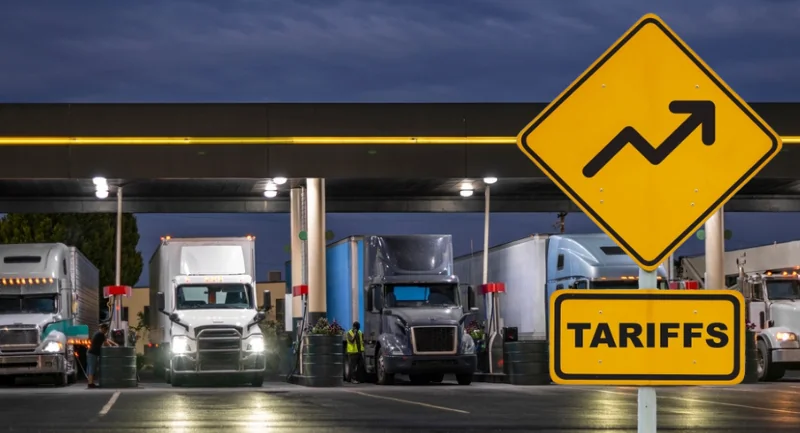 trucks parked at a fueling station with a yellow road sign that said tariffs