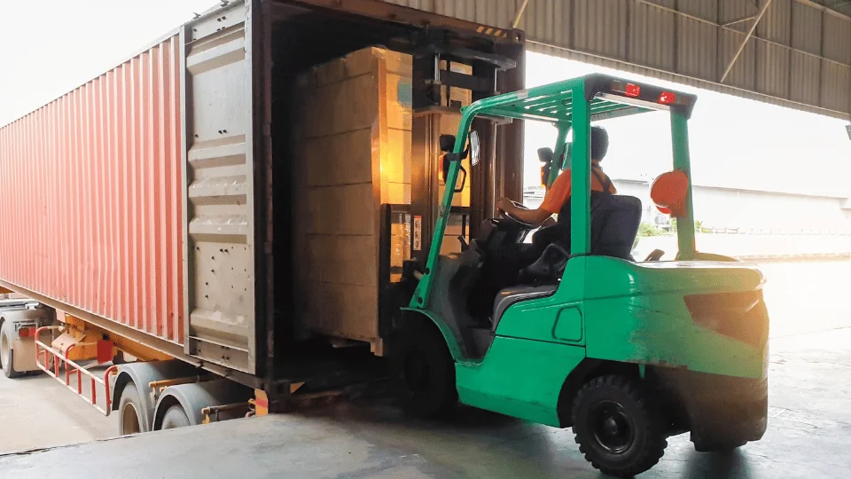 Moving Freight worker operating green forklift loading pallet of boxes into trailer