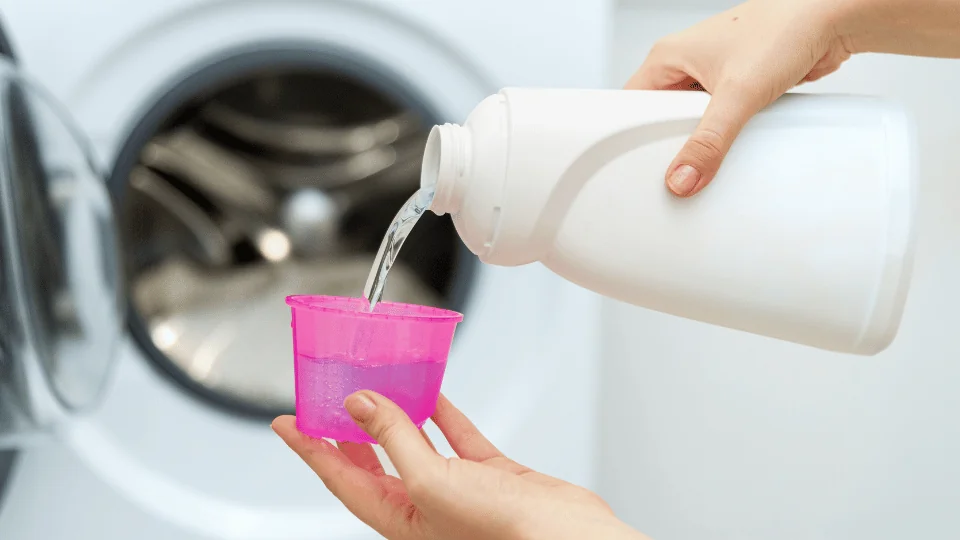 woman pouring liquid laundry detergent into plastic pink cup