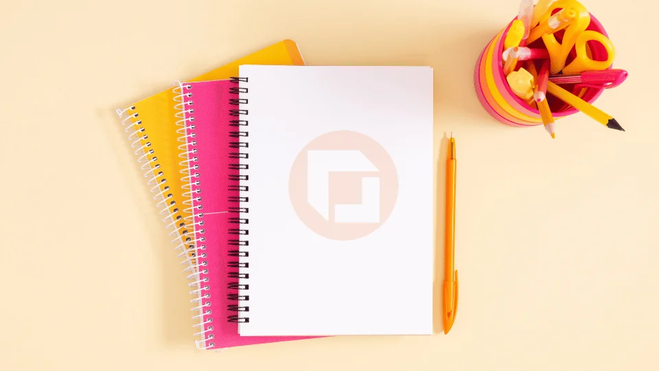 small stack of notebooks with the top notebook open next to a cup of art supplies